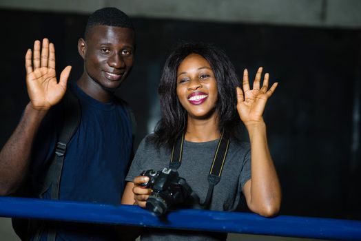 concept of gesture and people - happy young couple of tourists waving them standing in the city