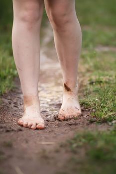 Barefoot girl walks through a puddles of water after the summer rain in countryside.