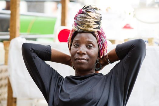 portrait of African woman with a scarf sitting in a chair behind her sales display