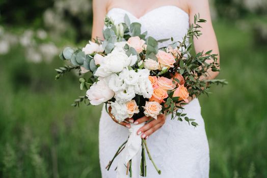 bride in a white dress with a large spring bouquet in a green forest