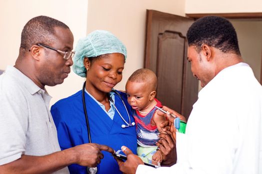 The doctor explains something to the baby's father while the nurse holds the baby in her arms.