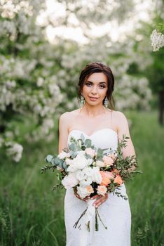 bride in a white dress with a large spring bouquet in a green forest