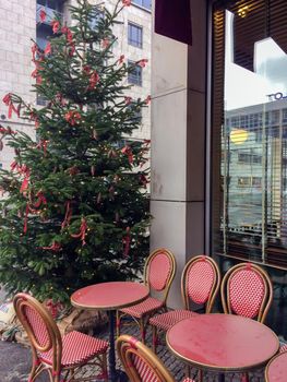 Street cafe near Christmas tree with red ornaments outside. Cozy wooden tables and chairs with warm plaid at winter market in old town. High quality photo