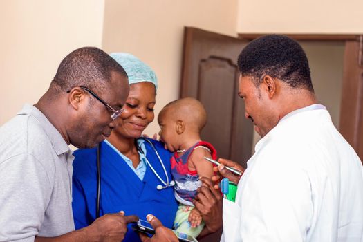 The doctor explains something to the baby's father while the nurse holds the baby in her arms.