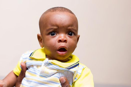 Close up of baby in his dad's arms sitting in the couch at home watching the camera surprised