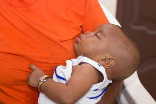 baby sleeping in his mother's arms sitting in a white chair.