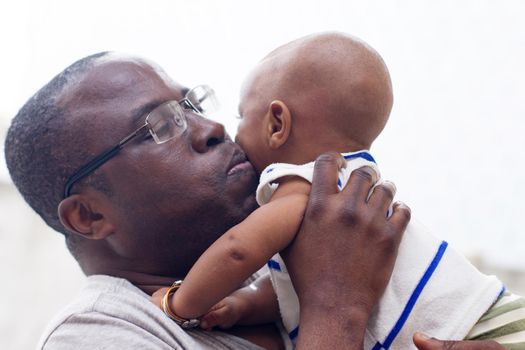 a young man standing in glasses and gray tee shirt kissing his baby.