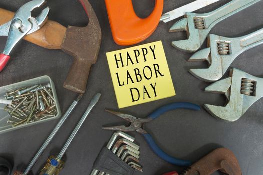 Happy labor day text on yellow notepad with repair equipment and many handy tools on a dark background