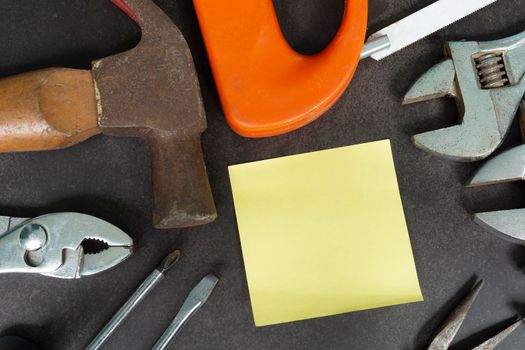 Labor day background concept. Yellow note sticker with repair equipment and many handy tools on a dark background. Top view with copy space for use and design