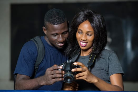 young happy tourist couple sitting back against an iron bar and looking at pictures together on their camera