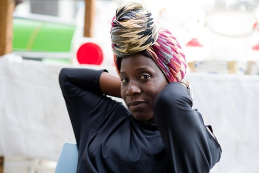 106/5000portrait of smiling african woman with a nice head scarf sitting behind her sales stand
