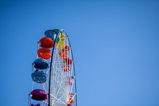 A large Ferris wheel against a blue sky. Booths with people go up. There is a place for the text. Concept: entertainment on summer holidays, holidays with children on weekends, ride on rides.