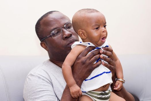 father and baby having fun at home. Proud African father holding an infant in arms while playing.