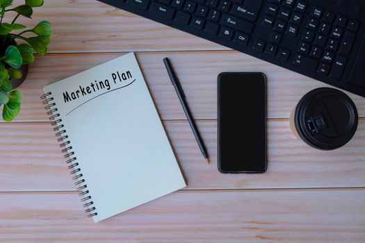 Marketing plan label on notepad with smartphone, coffee, pen and keyboard on wooden table. Business concept