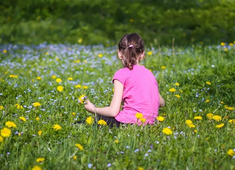 A girl on the green spring meadow with a lot of wildflowers in sunlight. Child exploring nature.