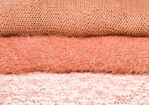 Pile of warm autumn and winter knitted sweaters on a home wardrobe shelf. Clothes in shades of living coral.