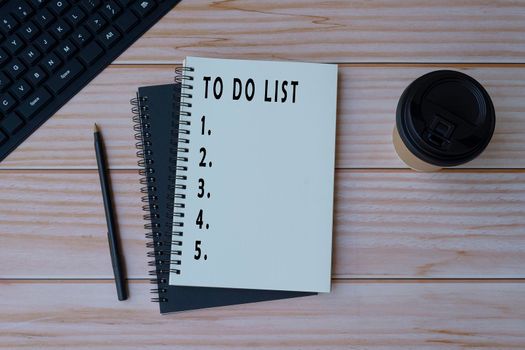 Text on notepad with pen, note book, keyboard and coffee on wooden desk - To do list