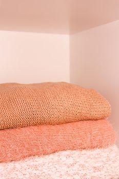 Pile of warm autumn and winter knitted sweaters on a home wardrobe shelf. Modern fashion clothes in shades of living coral.
