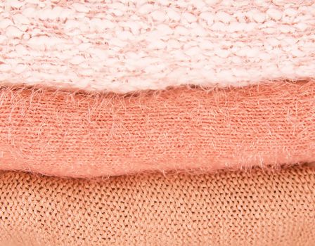 Pile of warm autumn and winter knitted sweaters on a home wardrobe shelf. Modern fashion clothes in shades of living coral.