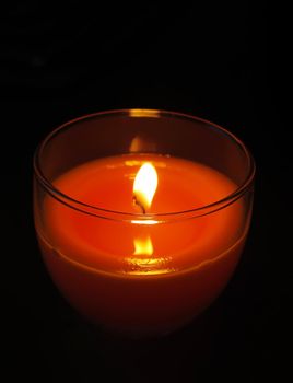 Red candle in transparent glass candlestick burning in darkness