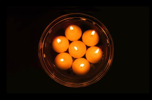 Small round decorative candles swimming in water in transparent cup on dark background