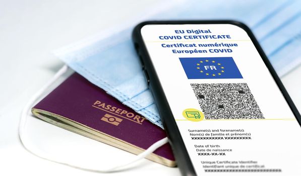 French EU Digital COVID Certificate with the QR code on the screen of a mobile phone over a surgical mask and a french passport. Immunity from Covid-19. Travel without restrictions.