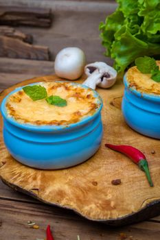 Pots with mushroom julienne on a wooden board, decorated with herbs. Julienne in cocotte with yellow cheese crust.
